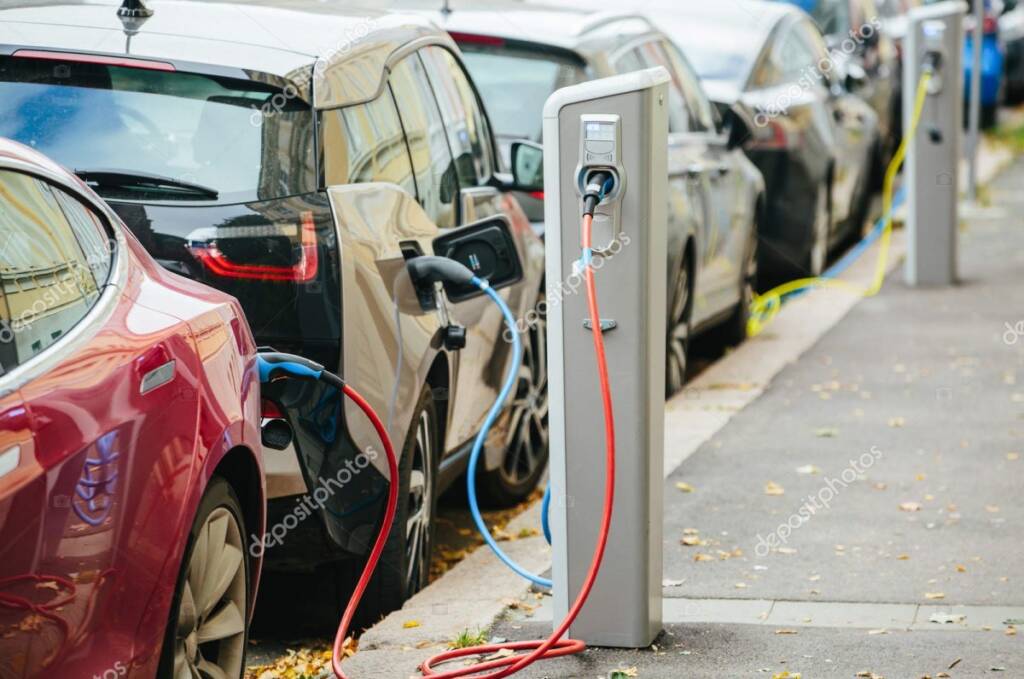 Color daytime photo of a long line of electric cars charging along a city sidewalk.