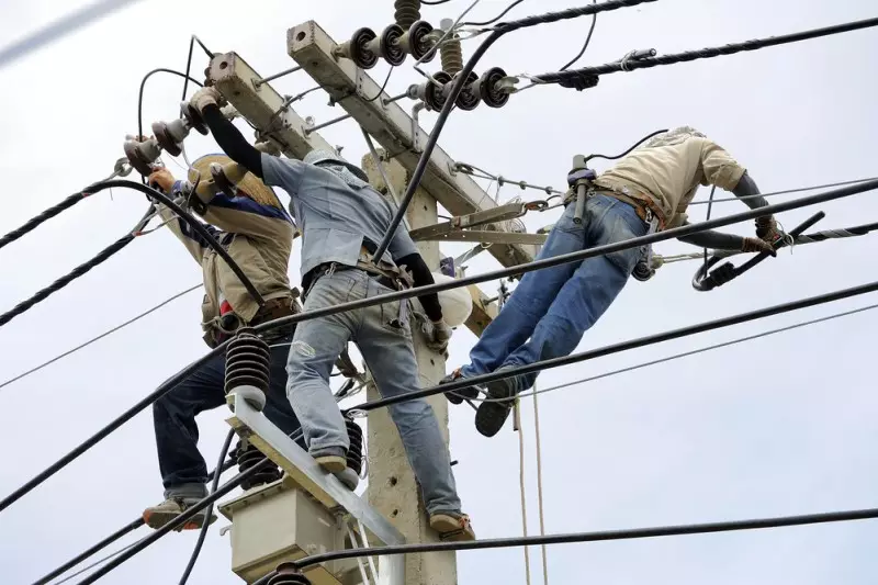 Color daytime photo facing the sky of a team of electrical linemen on power a pole working on high voltage power lines.
