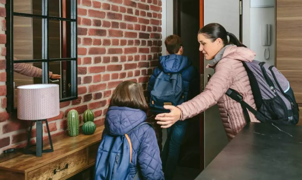 A color photo of a mother and her two children with emergency backpacks exiting their home's front door quickly.