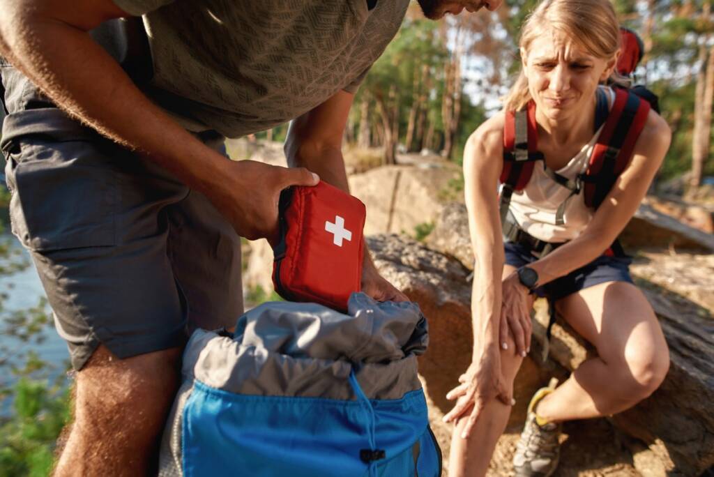 Color outdoor daytime photo of a young man using first aid kit on injured woman in the woods.