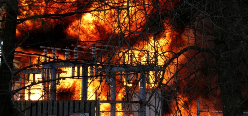 Color photo of a huge electrical grid transformer station fire with large bellowing yellow and red flames.